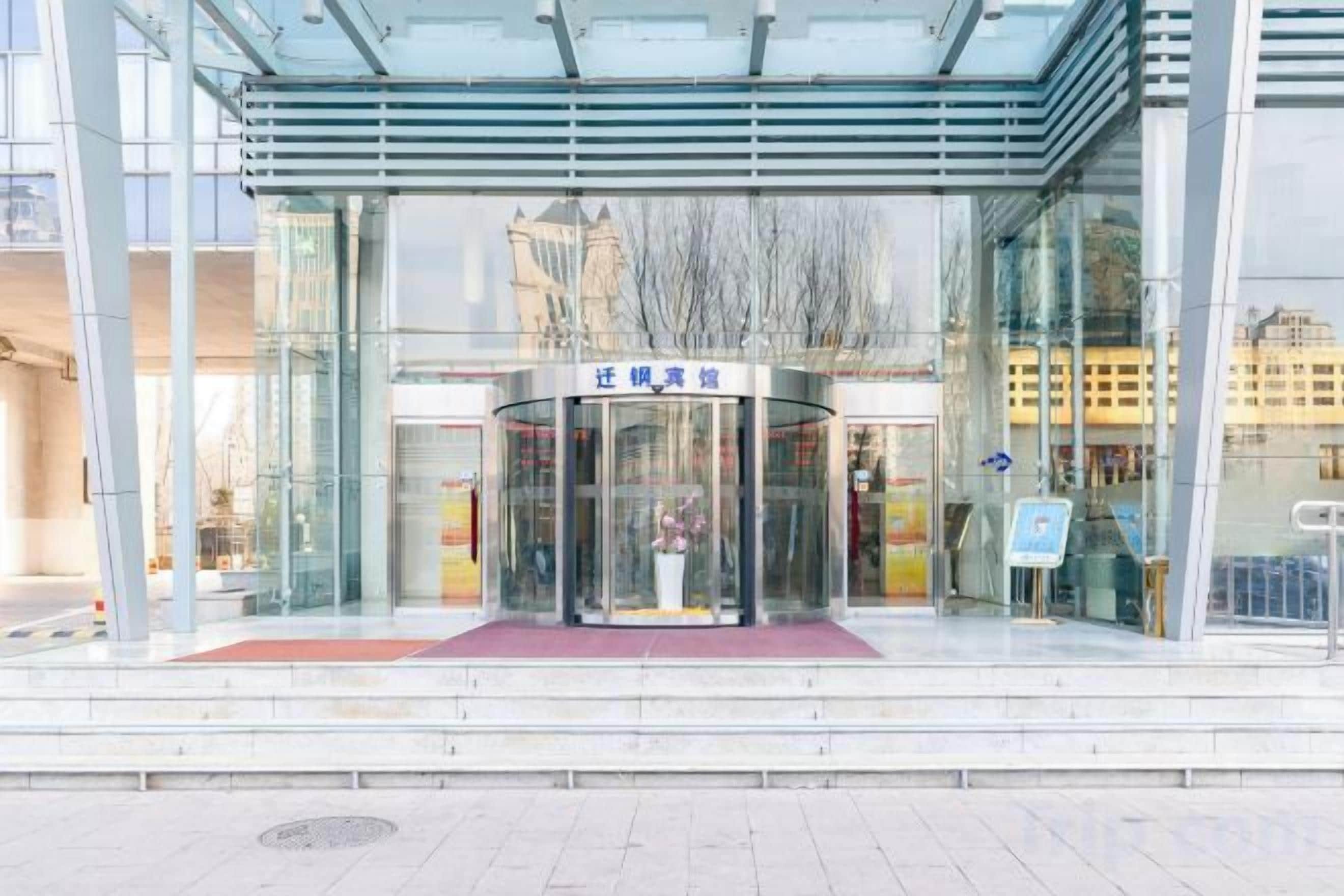 A modern building entrance with a glass facade, a revolving door, and a red carpet leading to the entrance.