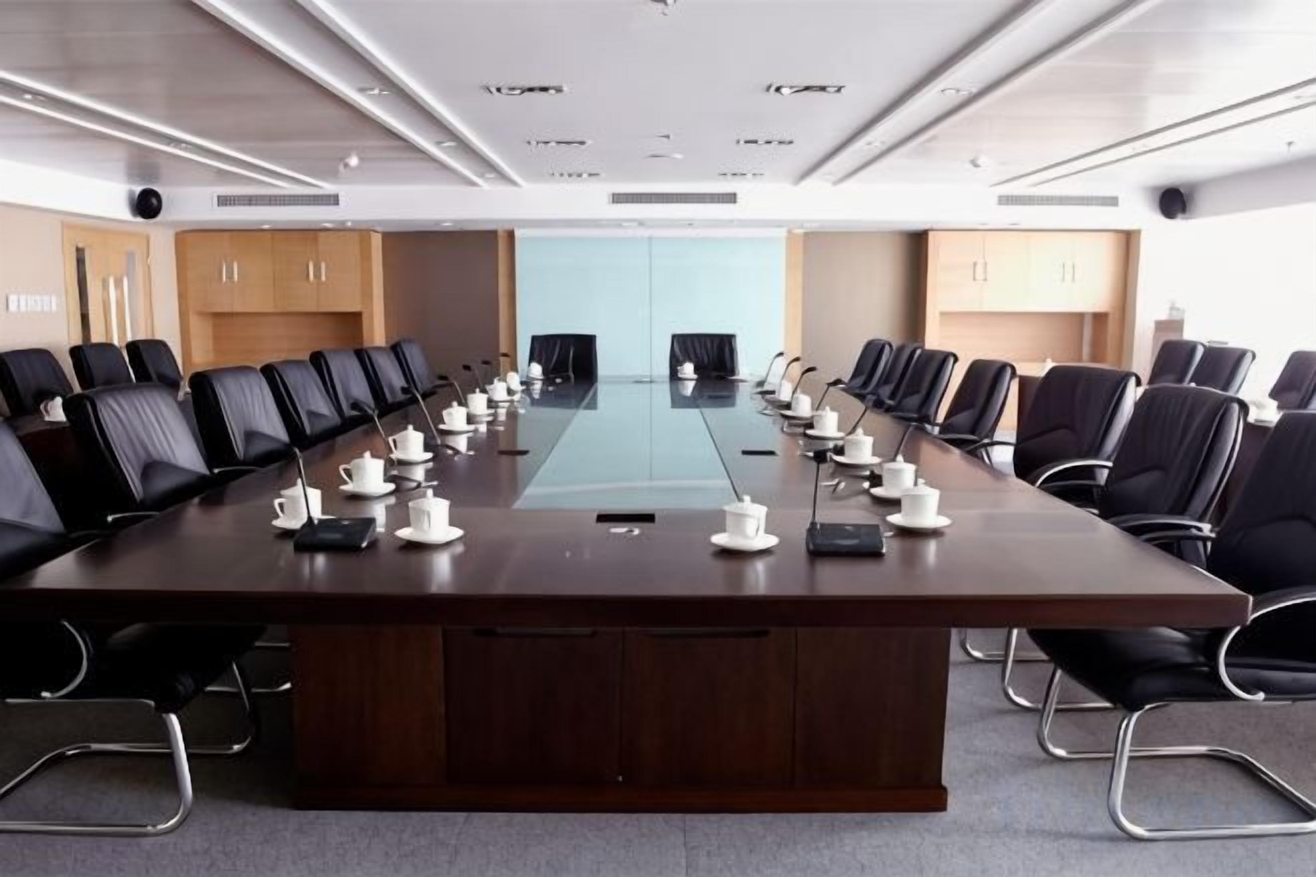 A conference room with a long table, black chairs, and a glass partition.