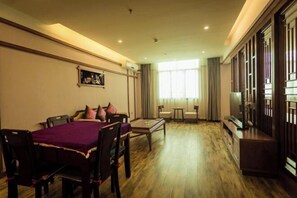 A spacious living room with a wooden floor, a dining table with chairs, a sofa with cushions, a TV, and a large window with curtains. - Hongzhi Hotel (Xingren)