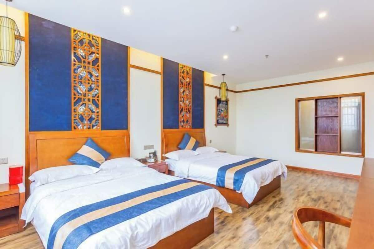A hotel room with two beds, wooden headboards, a wooden floor, and a window with frosted glass.