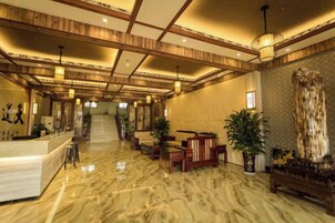 Un vestíbulo de hotel con piso de mármol, vigas de madera en el techo, una mesa de recepción, zonas de estar y plantas en macetas.