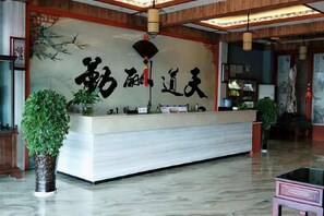 A reception desk with a marble top, a large calligraphy piece on the wall, and a hanging light fixture. - Hongzhi Hotel (Xingren)