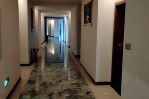 Un pasillo con piso de mármol, puertas a la derecha y un bote de basura a la izquierda.