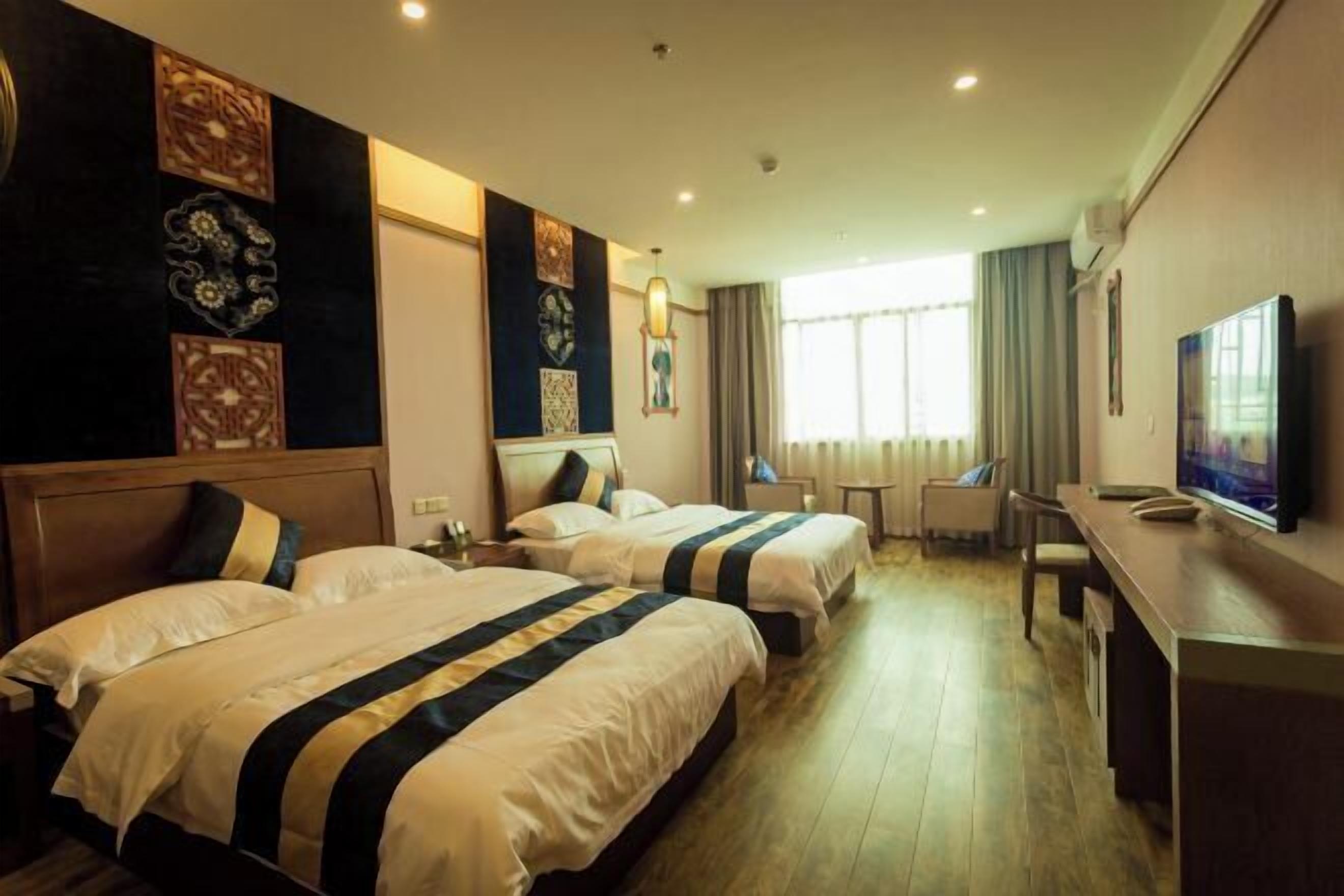 A hotel room with two beds, a desk, a television, and decorative wall panels.