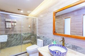 A modern bathroom with a glass shower enclosure, a white toilet, a marble-tiled vanity with a blue and white bowl sink, and a large mirror with a wooden frame. - Hongzhi Hotel (Xingren)