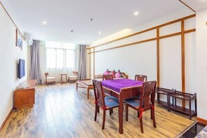 A hotel room with a wooden floor, a dining table with chairs, a sofa, a TV, and a window with curtains. - Hongzhi Hotel (Xingren)