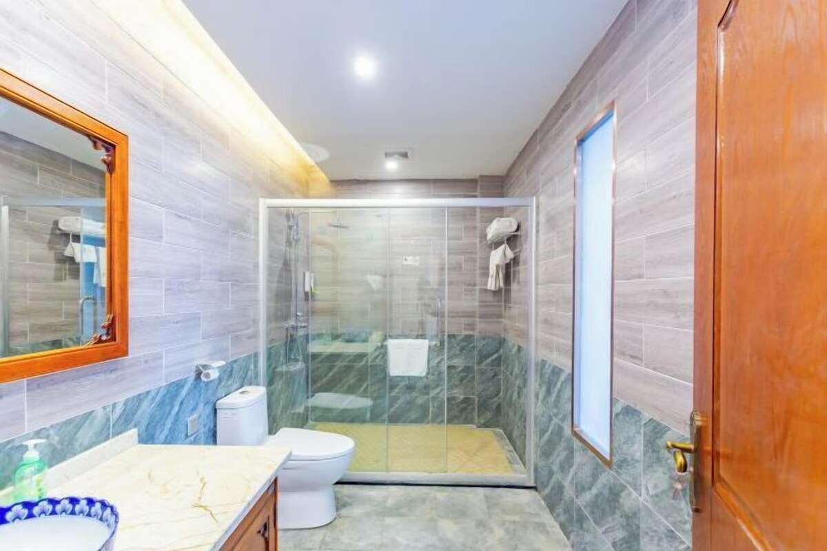 A bathroom with a glass-enclosed shower, a toilet, and a sink with a marble countertop.