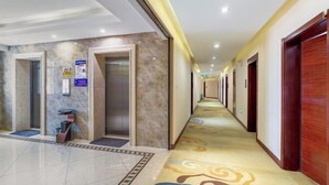 Un couloir d’hôtel avec un sol en marbre, des portes en bois et un tapis à motifs.