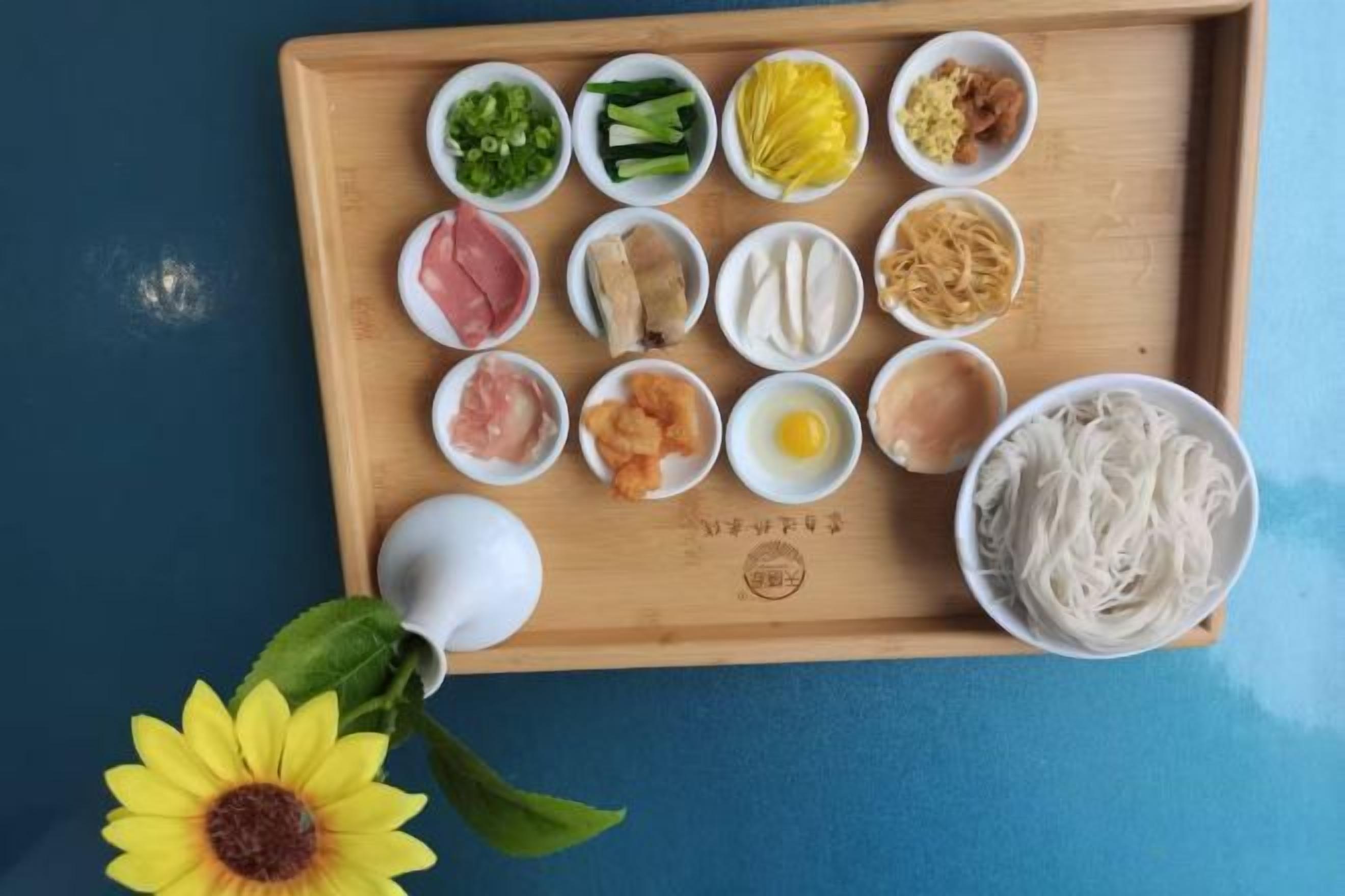 Uma bandeja de madeira com diversos alimentos e uma tigela de macarrão sobre uma superfície azul.