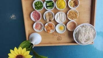 Uma bandeja de madeira com diversos alimentos e uma tigela de macarrão sobre uma superfície azul.