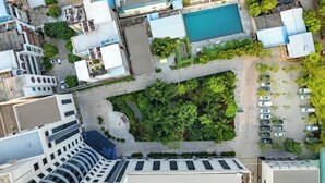 Vue aérienne d’un hôtel doté d’une piscine sur le toit, entouré de verdure et bordé d’un parking.