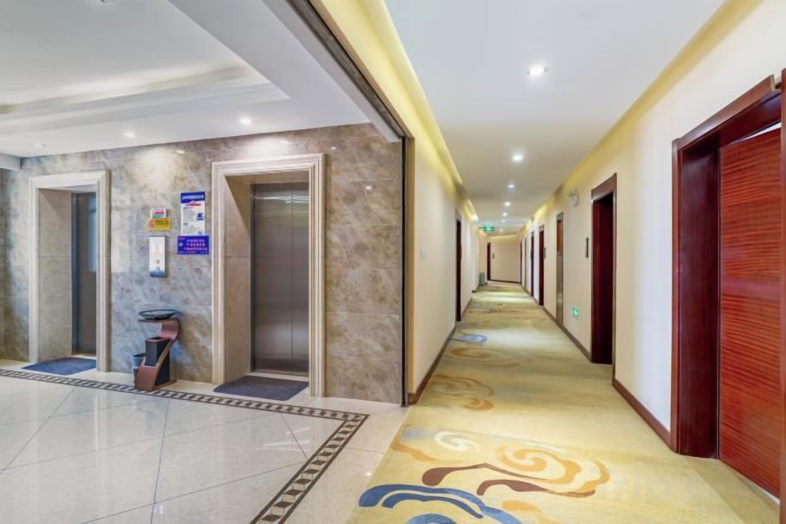 A hotel corridor with a marble floor, wooden doors, and a patterned carpet.