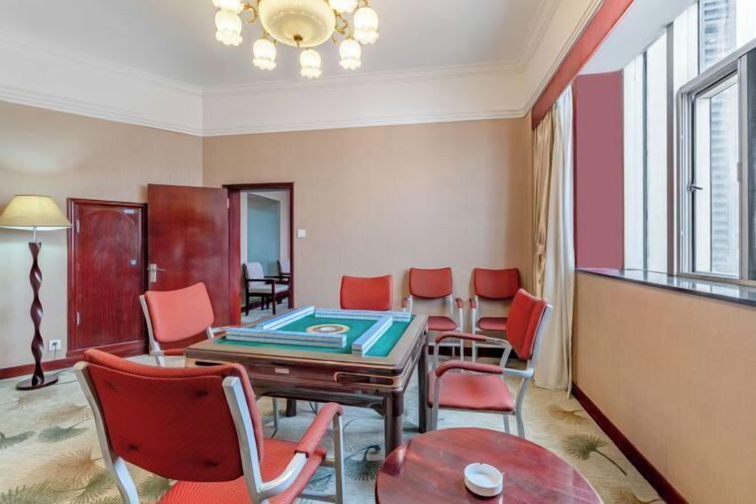 A conference room with a large table, red chairs, a chandelier, and a view of the city through large windows.