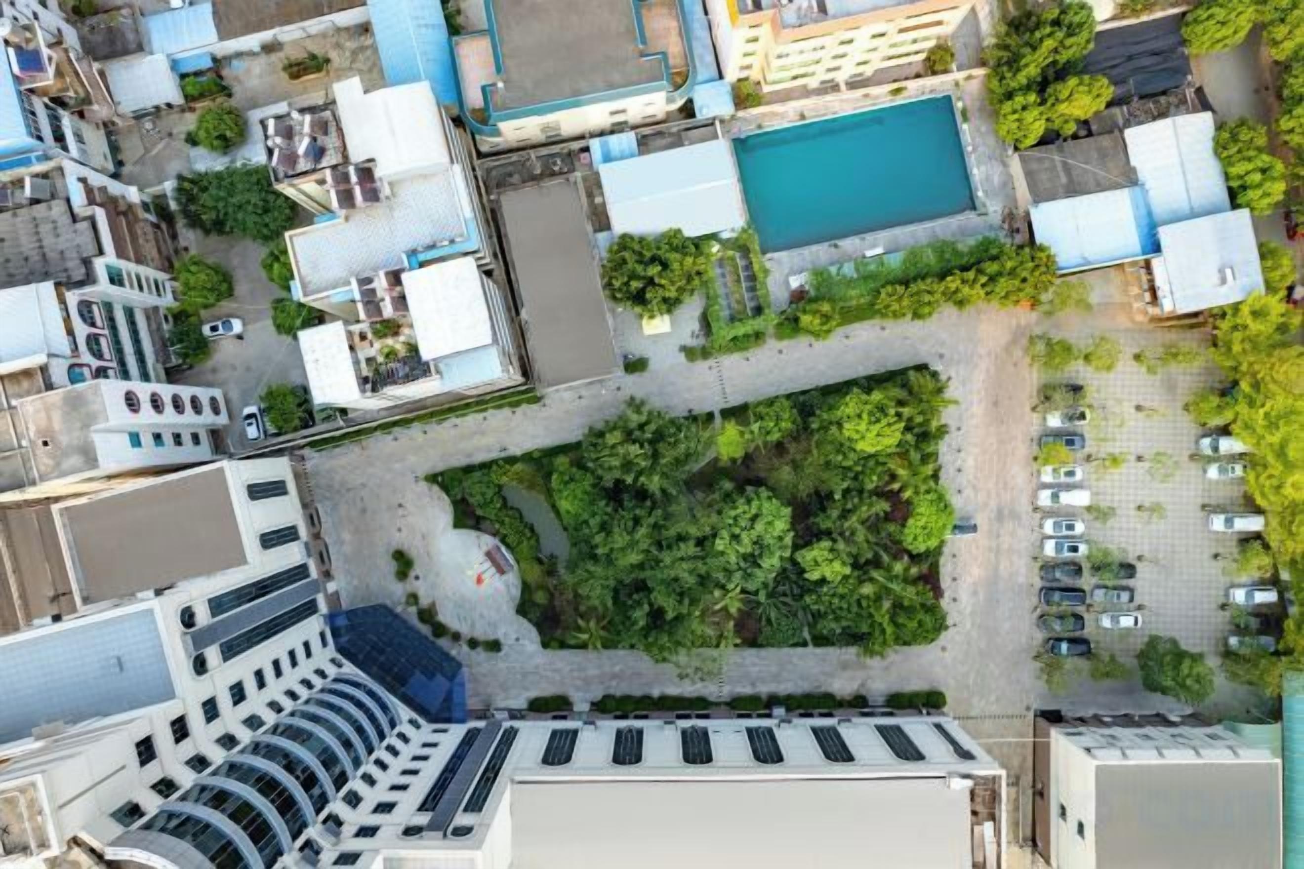An aerial view of a parking lot with a swimming pool, surrounded by buildings and greenery.