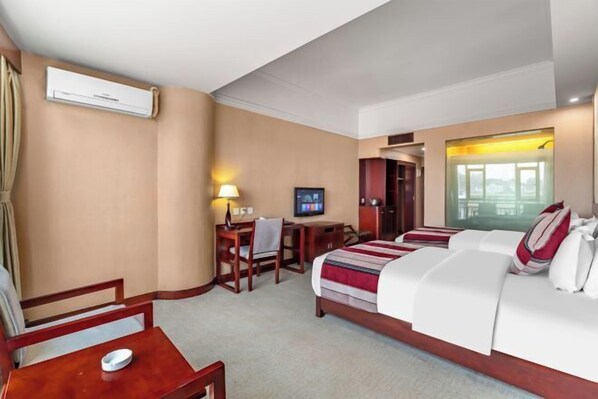 A hotel room with a bed, desk, chair, TV, and an air conditioning unit.