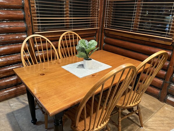 Uma mesa de jantar de madeira com quatro cadeiras, um vaso de planta e um jogo de mesa estampado.