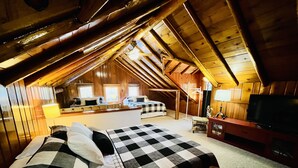 A cozy attic bedroom with a checkered bed, a television, and a desk area with a lamp. - Cozy Log Cabin on Golf Course, Across from Otsego Lake (Gaylord)