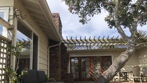 Ein überdachter Patio-Bereich mit Holzdeck, gepolstertem Sitzplatz, einer Topfpflanze und einer Pergola.