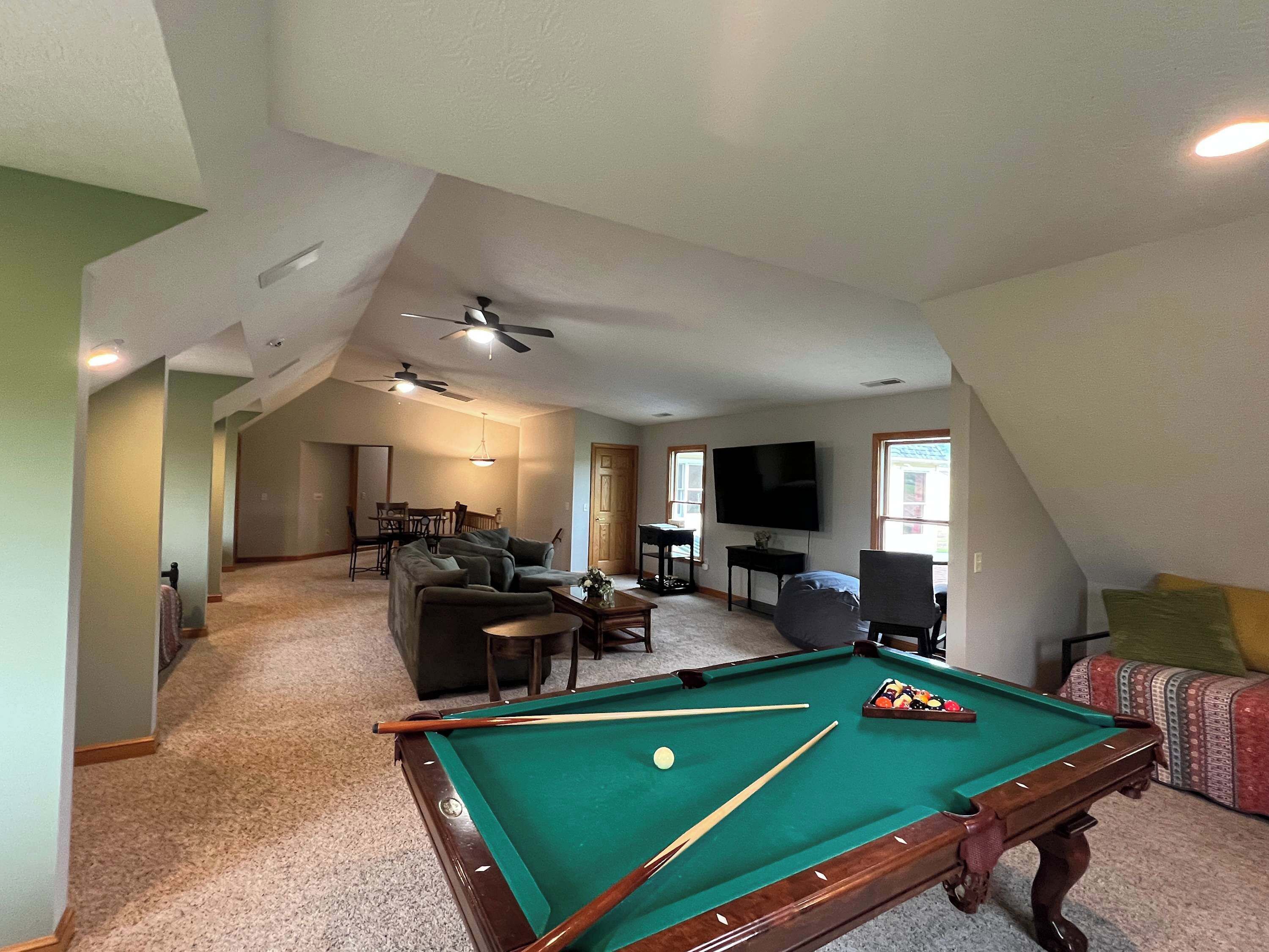 Un vaste salon doté d’une table de billard, de ventilateurs de plafond et d’un téléviseur fixé au mur.