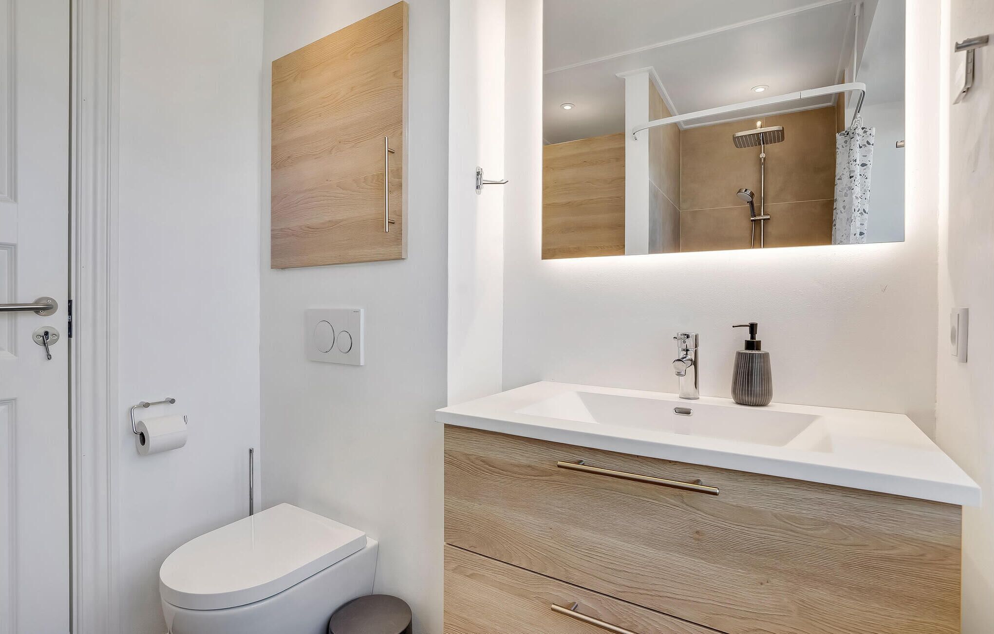 A modern bathroom with a white toilet, wooden vanity, and a mirror above the sink.