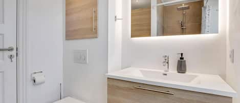 A modern bathroom with a white toilet, wooden vanity, and a mirror above the sink.