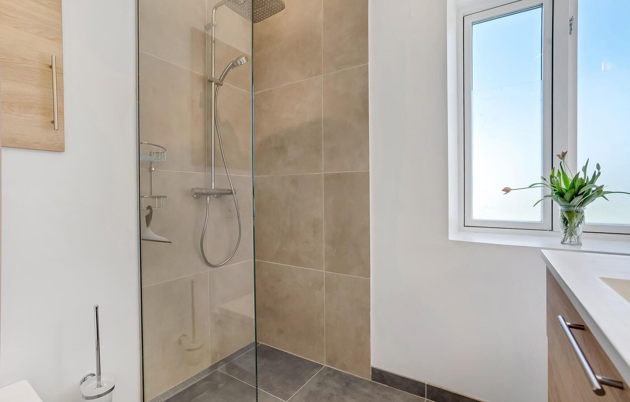 Un baño moderno con ducha envuelta en vidrio, un lavabo blanco y un ventanal con vistas.