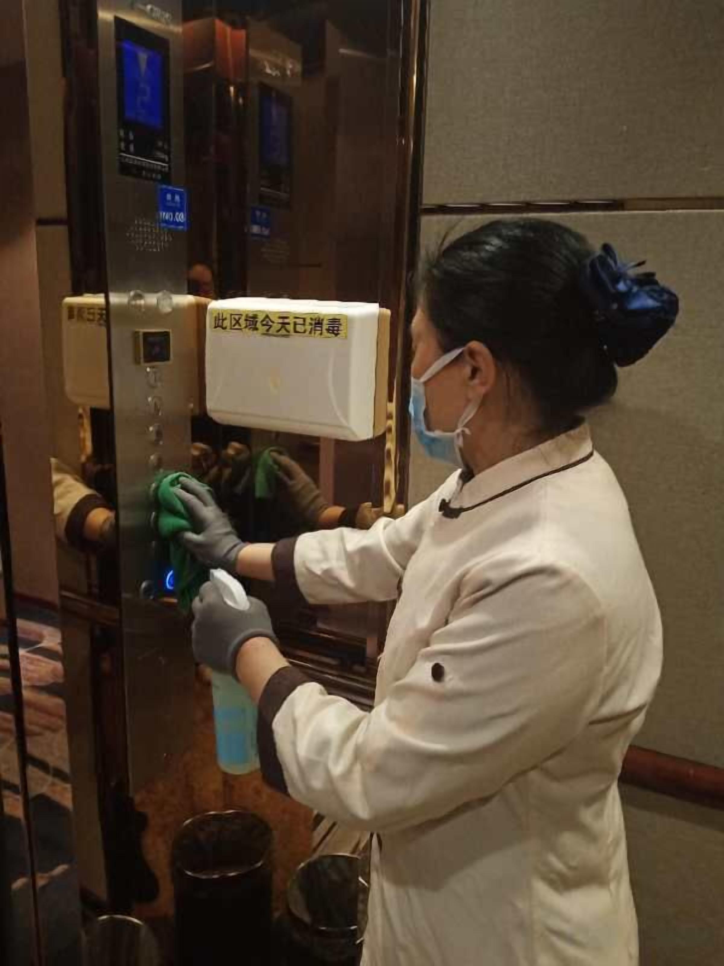 Una persona limpia una puerta de ascensor de vidrio con un atomizador y guantes.