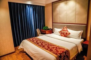 A hotel room with a large bed, a headboard, a desk with a chair, and a window with curtains.