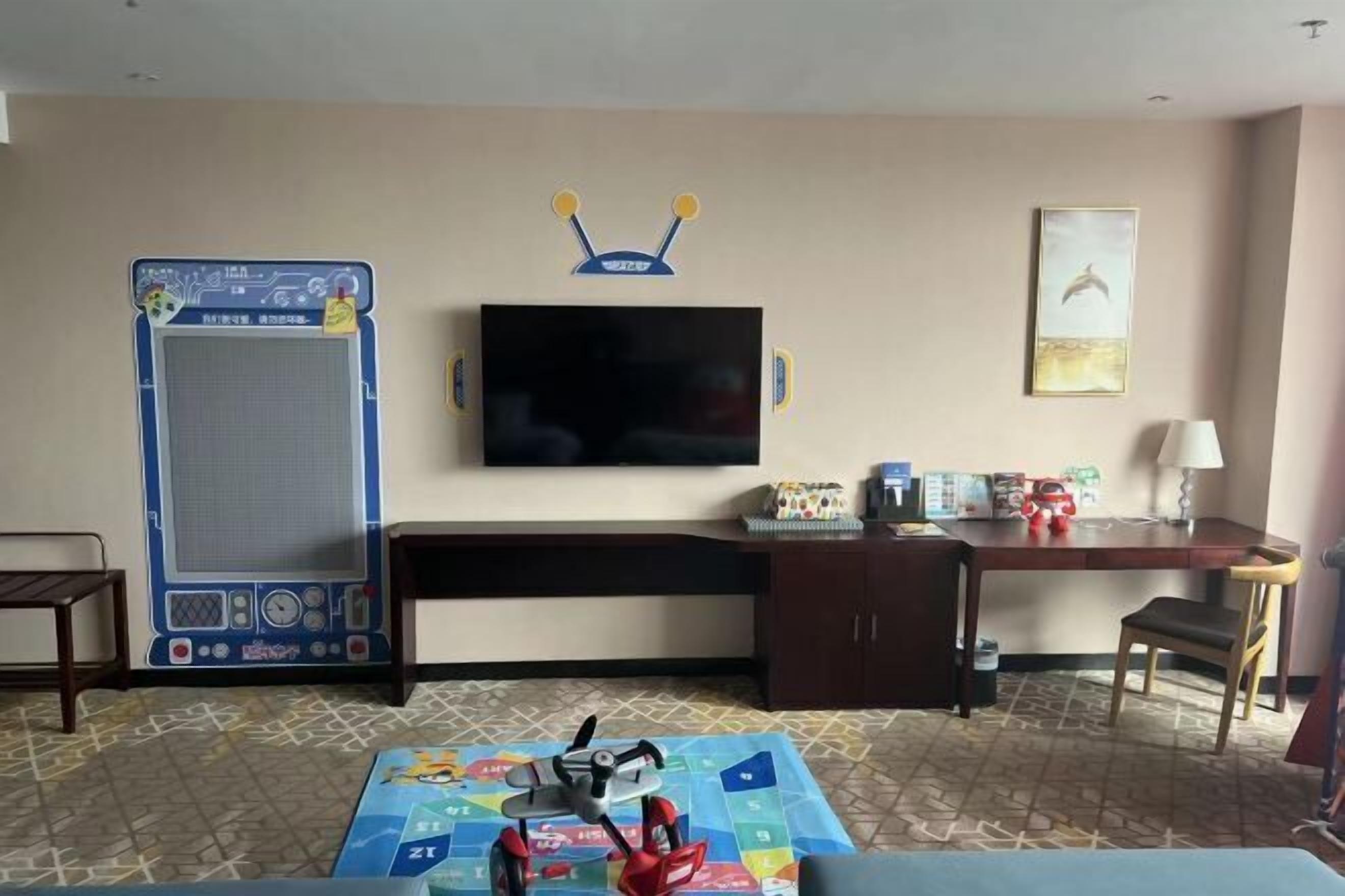 A hotel room with a television, a desk, a chair, a game table, and a large exercise machine.