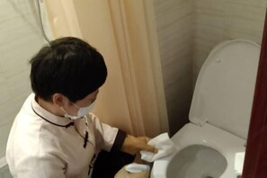 A person cleaning a toilet in a bathroom with beige walls and a shower curtain.