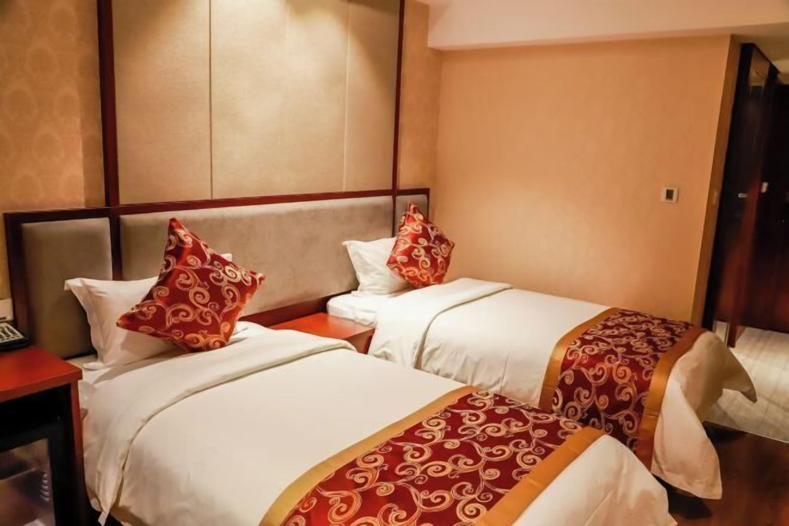 A hotel room with two beds, each with white linens and red patterned pillows.