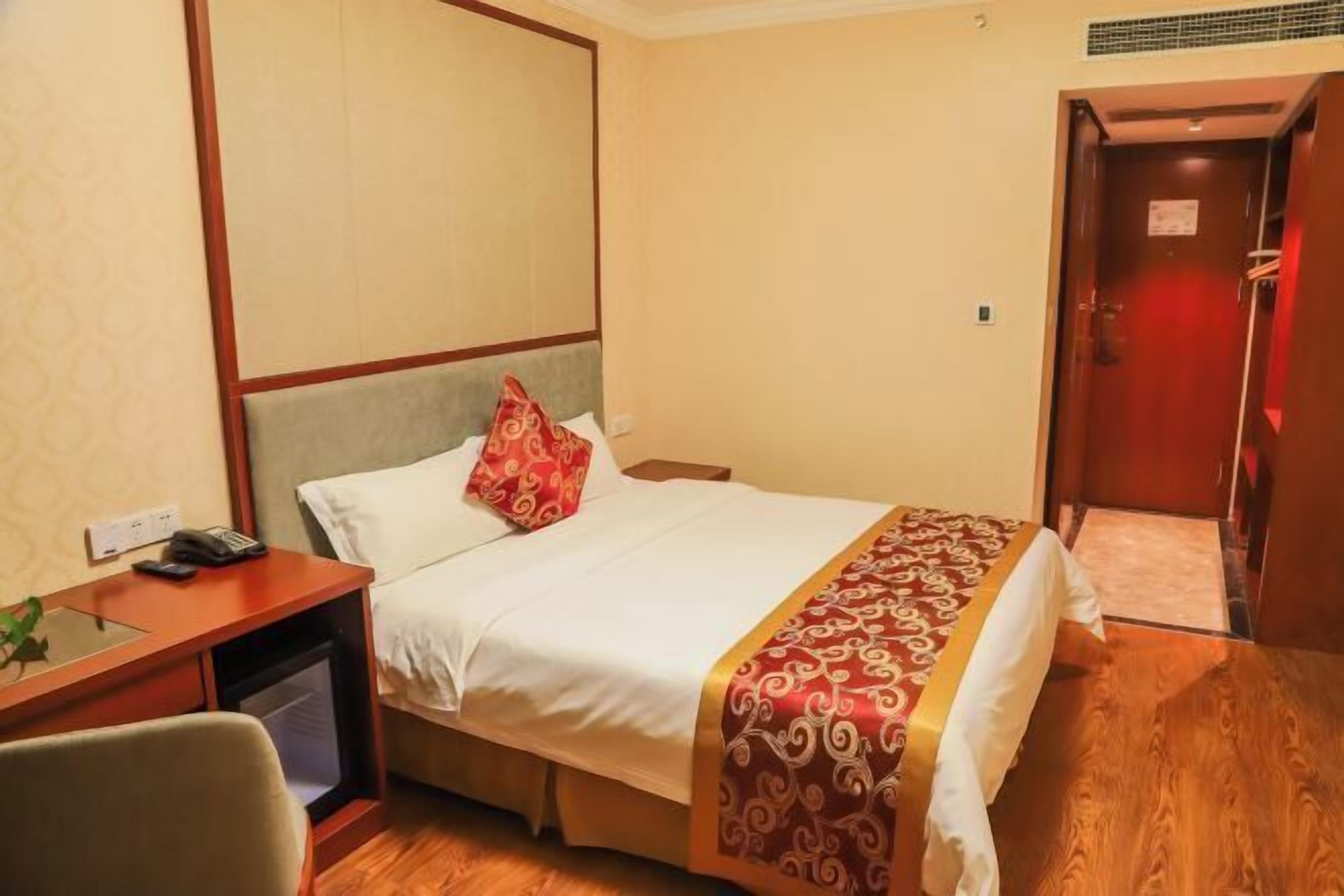 A hotel room with a bed, a desk with a telephone, and a door leading to a bathroom.