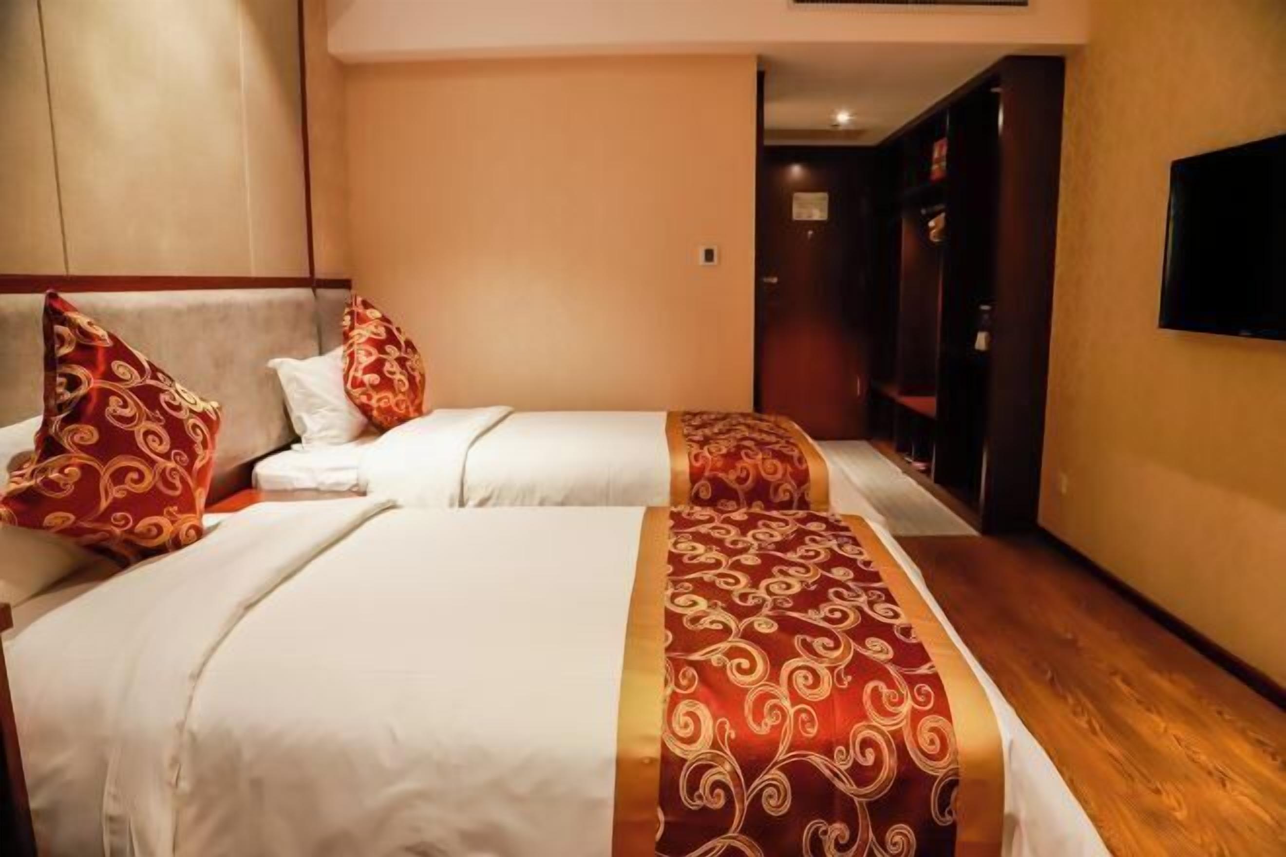 A hotel room with two beds, each with red and white bedding, and a television mounted on the wall.