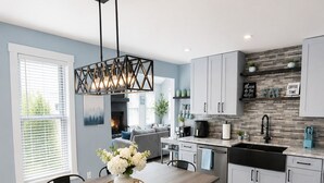 A modern kitchen with a dining area, featuring a wooden table, black chairs, a pendant light, and a backsplash with tiles. - Modern Poconos Cabin w/ Hot Tub Near Kalahari & CamelBack Mountain ! (Long Pond)