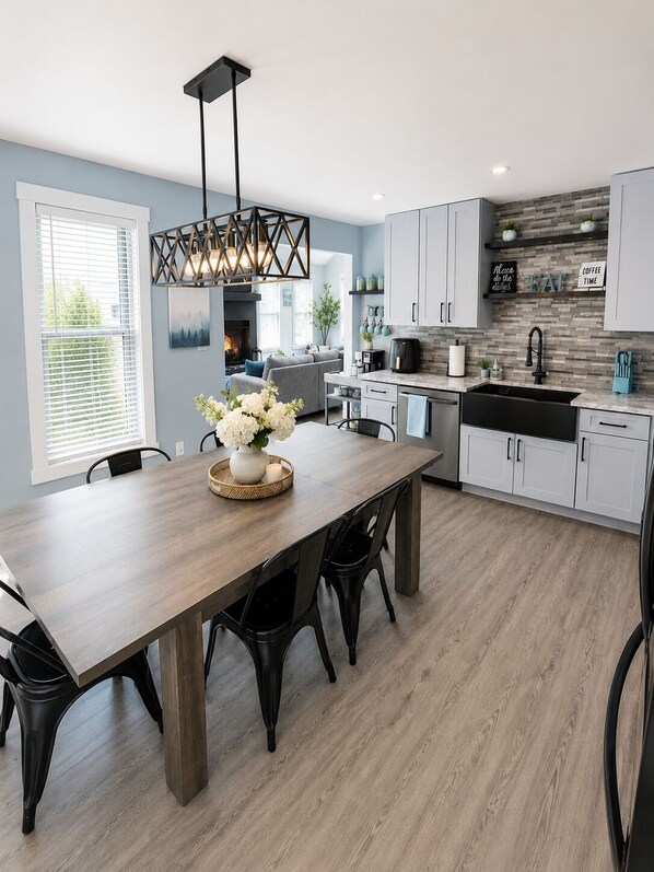 A modern kitchen with a dining area, featuring a wooden table, black chairs, a pendant light, and a backsplash with tiles. - Modern Poconos Cabin w/ Hot Tub Near Kalahari & CamelBack Mountain ! (Long Pond)