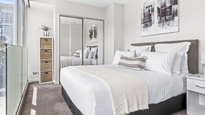 A modern bedroom with a large bed, a wardrobe, and a cityscape painting. - Light and convenient city living (Auckland)