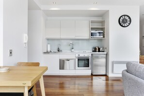 A modern kitchen with white cabinets, stainless steel appliances, a microwave, and a clock on the wall. - Light and convenient city living (Auckland)