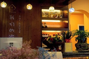 A reception area with a wooden wall, a reception desk, and a shelf with flowers and bottles. - Jiuqi Our House (Zhangjiajie)