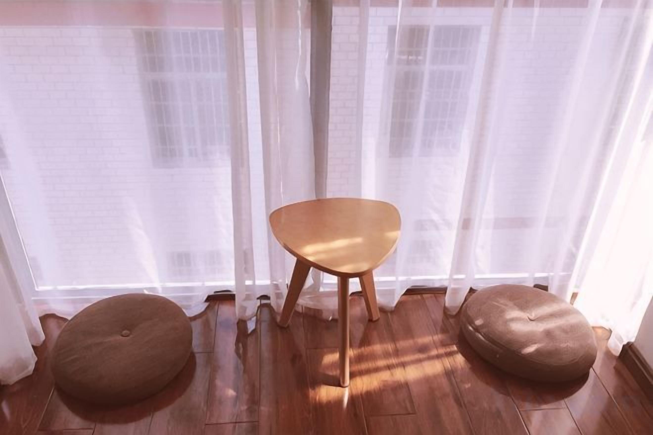 Una habitación con piso de madera, una silla de madera y dos otomanes redondos.