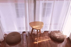 A room with a wooden floor, a wooden chair, and two round ottomans.