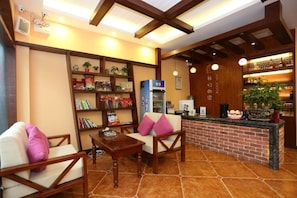 A hotel lobby with seating, a reception desk, a bookshelf, and a coffee machine. - Jiuqi Our House (Zhangjiajie)