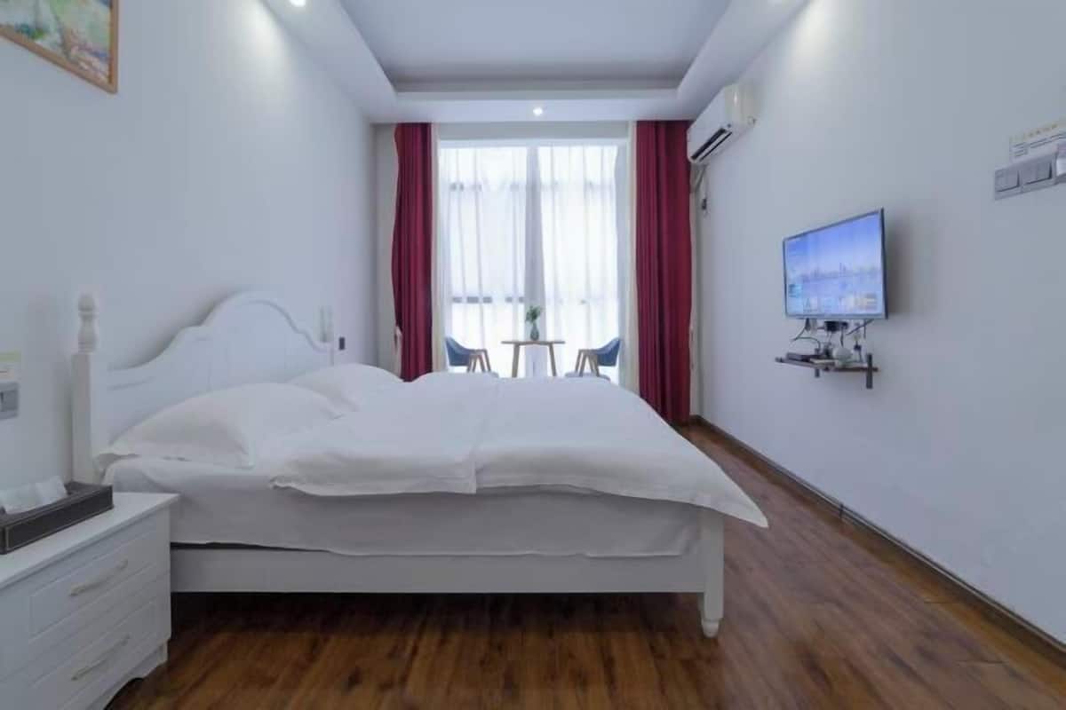 Een slaapkamer met een bed, nachtkastje, televisie en een raam met gordijnen.