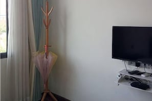 A room with a television on a stand, a coat rack with an umbrella, and a window with curtains. - Jiuqi Our House (Zhangjiajie)
