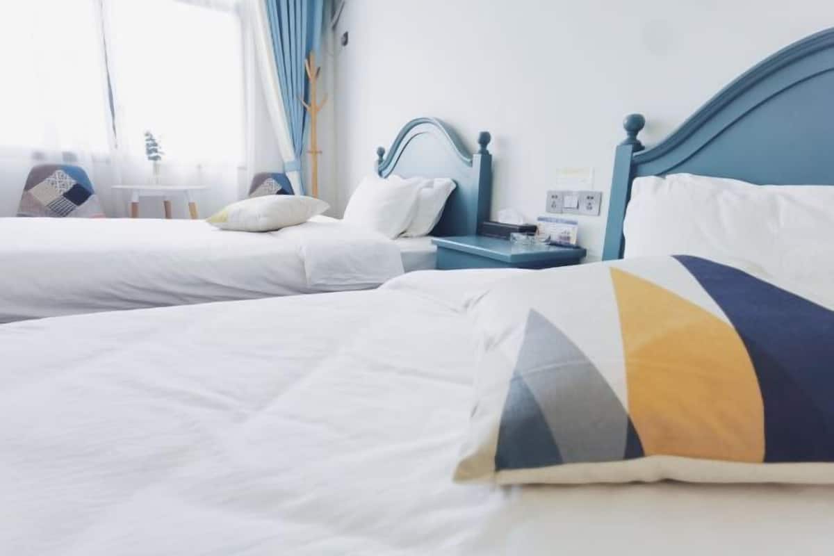Een hotelkamer met twee bedden, een nachtkastje, een lamp en een raam met gordijnen.