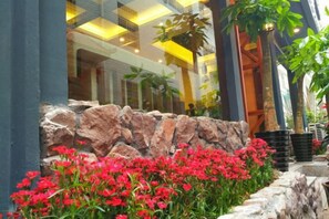 Un muro de piedra con flores rojas frente a un edificio con ventanas grandes y un balcón.