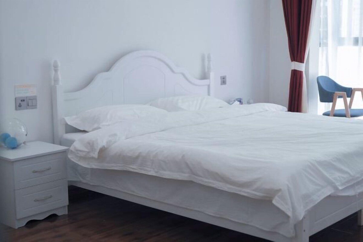 Een wit bed met een houten hoofdbord, een witte nachtkastje met lades, en een blauwe stoel.