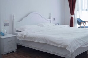 Een wit bed met een houten hoofdbord, een witte nachtkastje met lades, en een blauwe stoel.