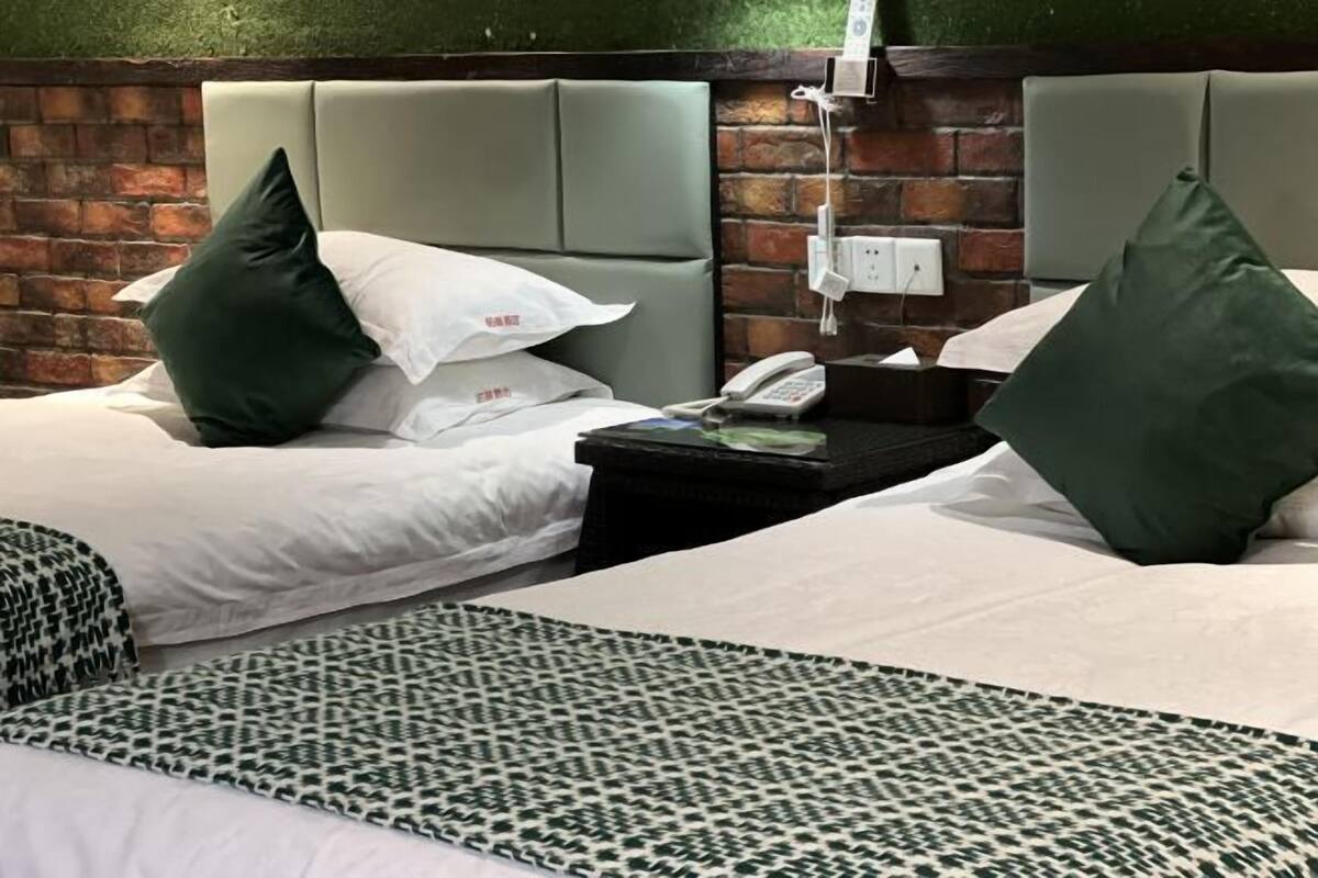 A hotel room with two beds, each with a pillow and a bedside table with a phone and a lamp.