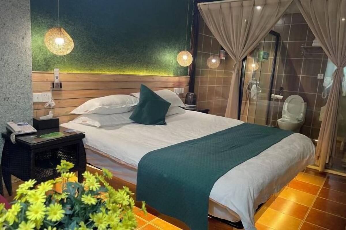 A neatly made bed with a green throw blanket, a bedside table with a lamp, and a small plant on the floor.