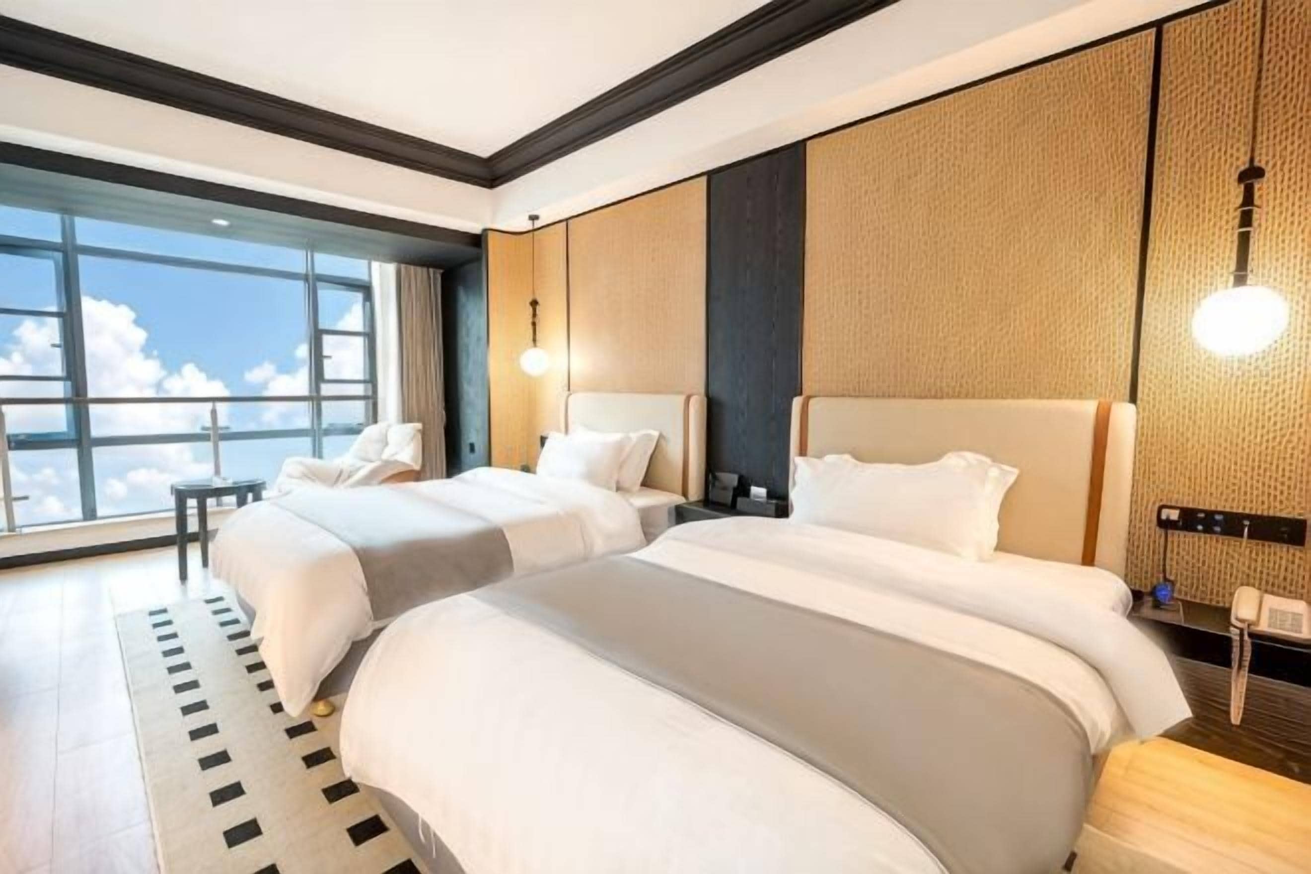 A hotel room with two beds, a large window, and a view of the sky.